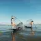 Two people wearing traditional rice hats on small fishing boats with large cages and oars against the blue sky © Unsplash