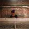 Woman weaving textiles against a red brick wall © Pexels