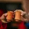 Two people holding two clay cups in their hands and holding them together to cheers